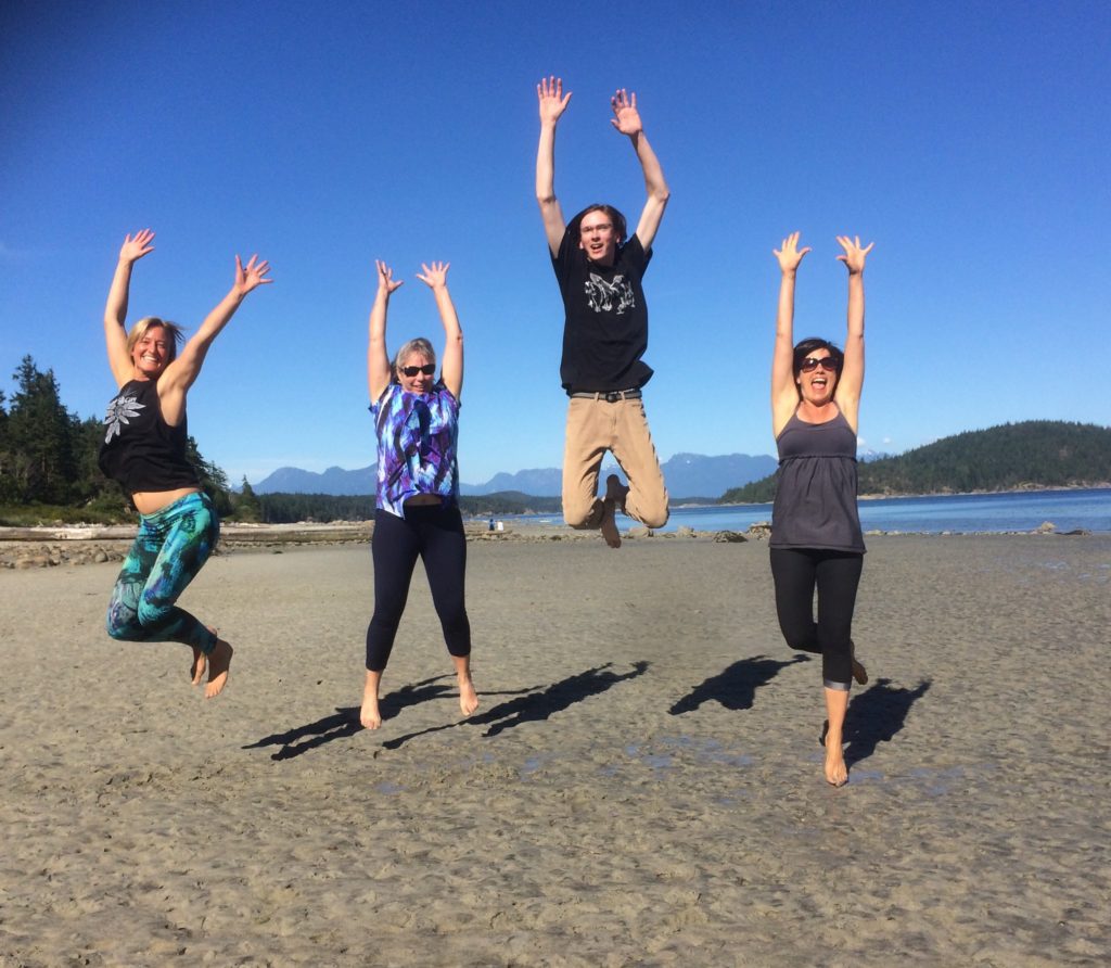Four guys jumping and raising their hands on the Cortes Island beach